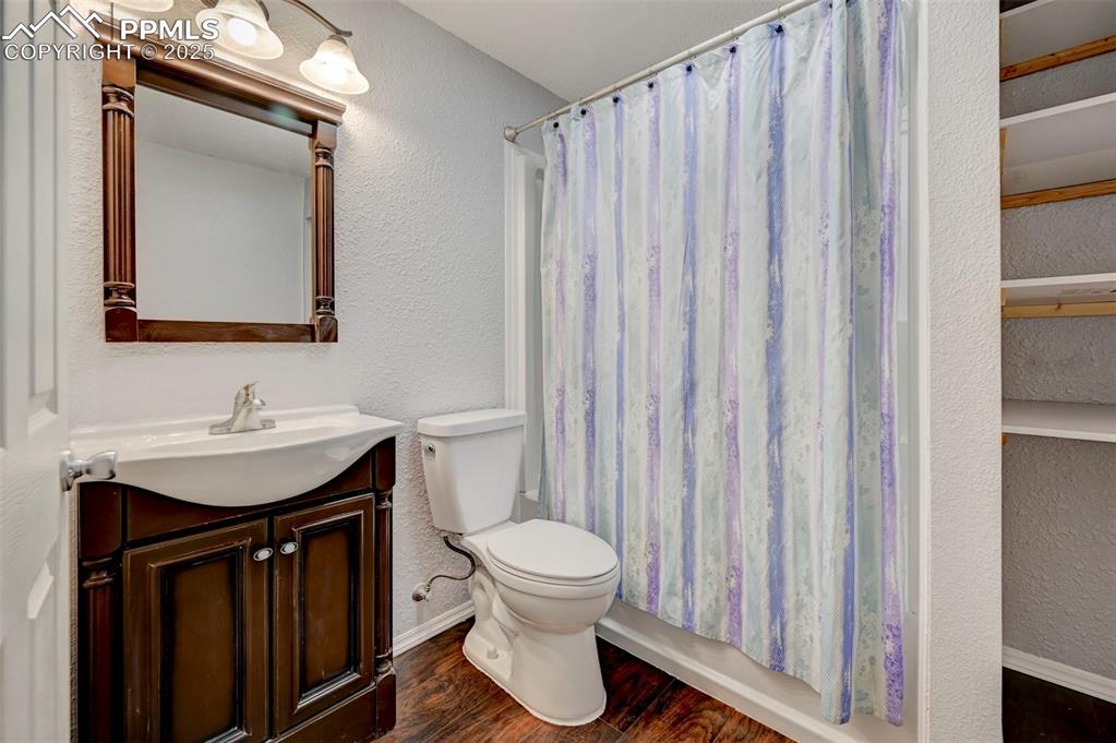 Image 30 of 37: Bathroom with vanity, wood finished floors, baseboards, toilet, and a textu