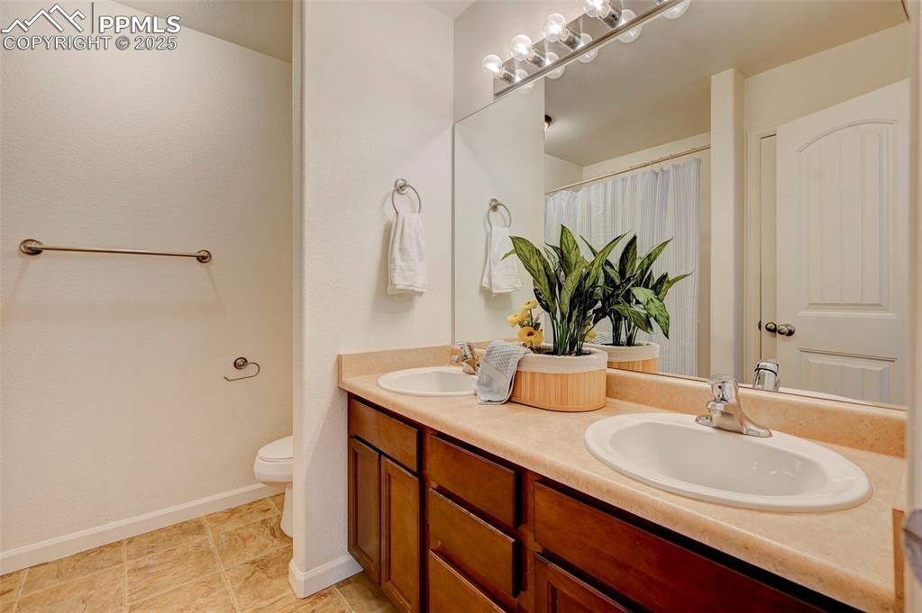 Image 34 of 37: Bathroom with double vanity, toilet, baseboards, and a sink