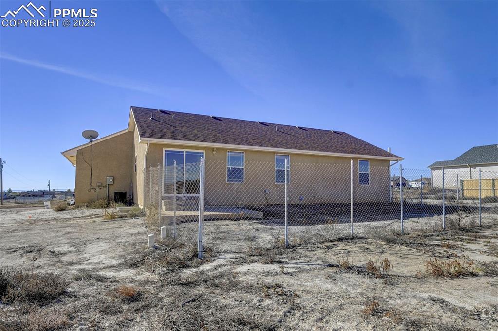 Image 36 of 37: Back of house featuring stucco siding, roof with shingles, and fence