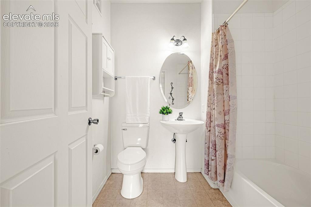 Image 13 of 27: Pedestal sink with chrome fixtures, oval wall mirror, and overhead vanity l
