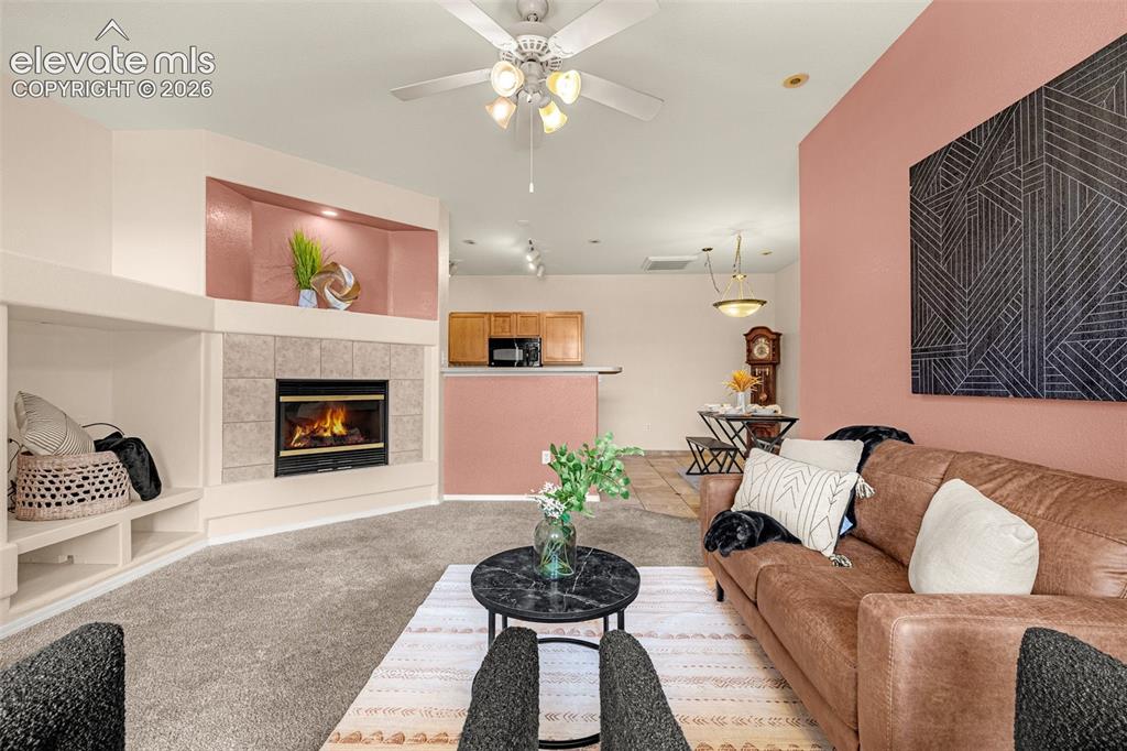 Image 4 of 27: Carpeted living area with a ceiling fan, fireplace featuring a tile surroun