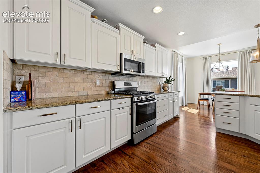 Image 13 of 50: White shaker-style cabinetry, stainless steel appliances, stone slab counte