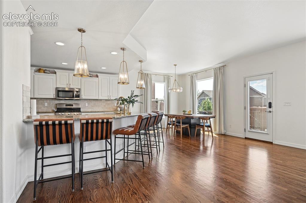 Image 20 of 50: Open-concept kitchen and dining area featuring wood-finish flooring, white 