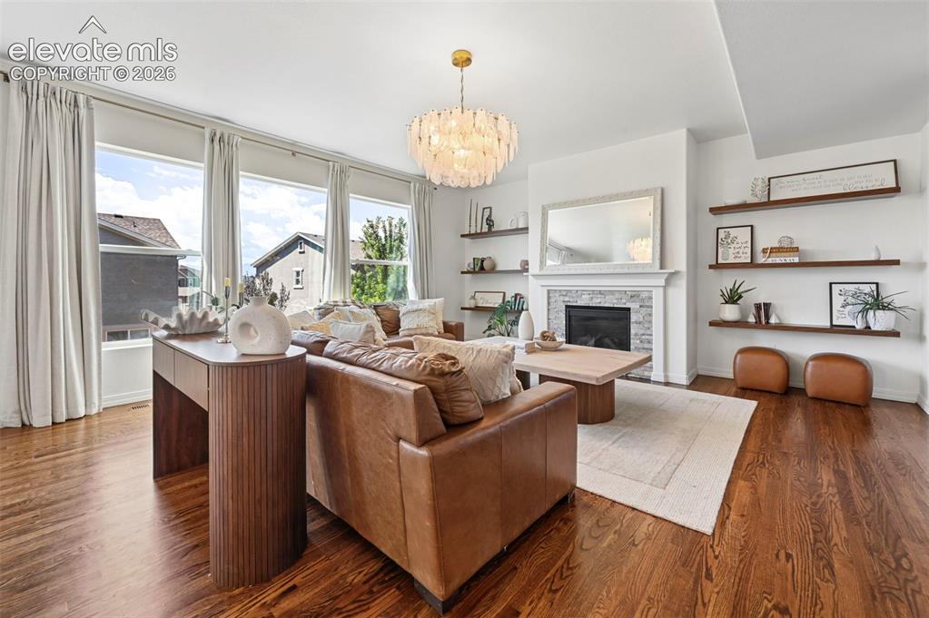 Image 3 of 50: Hardwood flooring, a fireplace with a stone surround, multiple large window