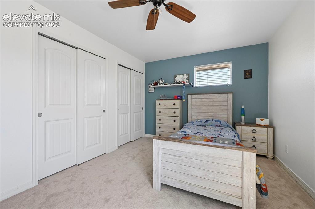 Image 37 of 50: Plush carpeting, ceiling fan with wood-finish blades, window with blinds, a