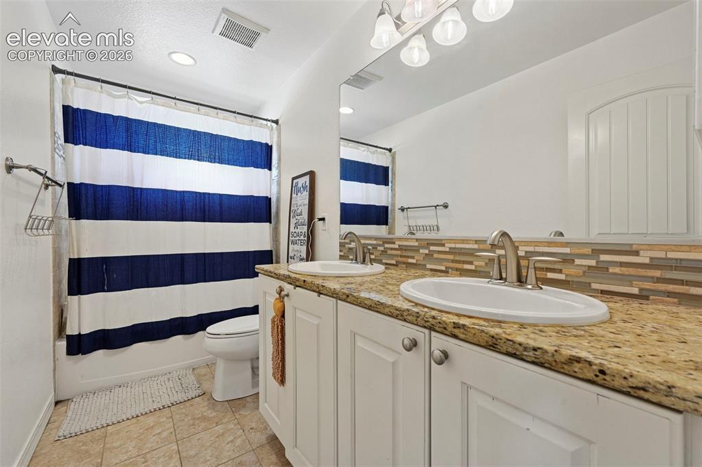 Image 38 of 50: Dual sink vanity with stone countertop, white shaker cabinetry, and brushed