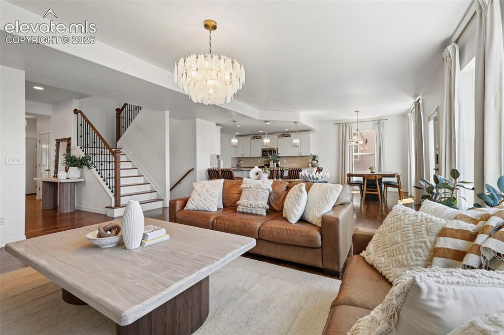 Image 5 of 50: Open-concept living area with wood-finish flooring, a contemporary chandeli