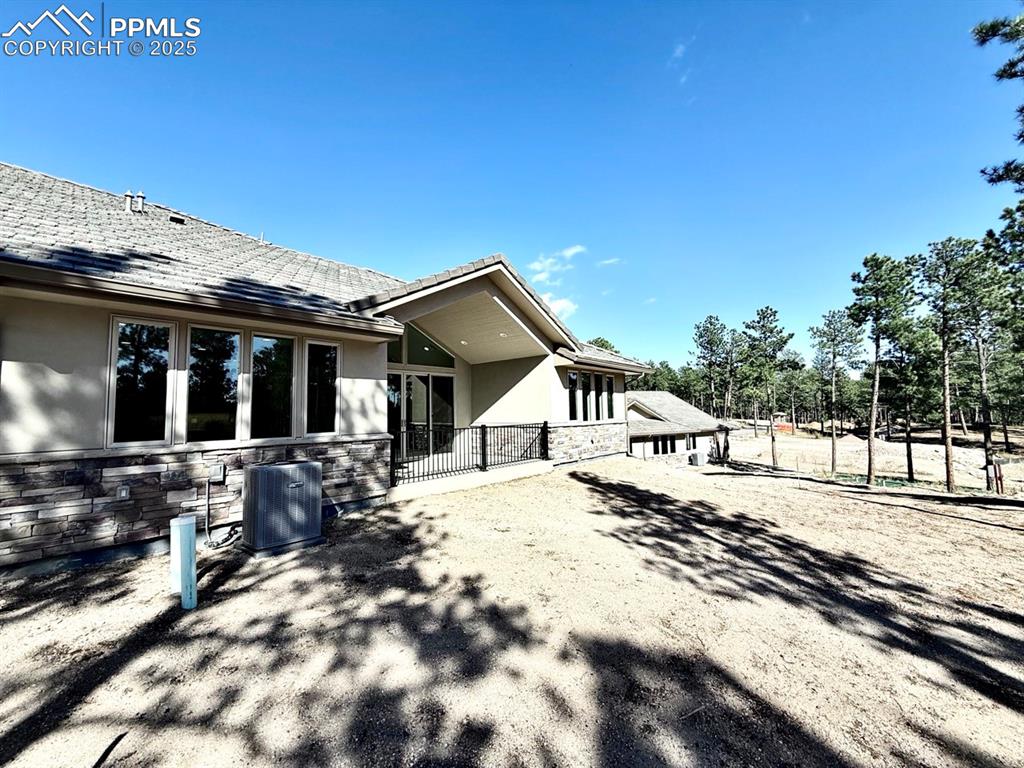 Image 30 of 32: Back of house with stucco siding, stone siding, and a patio area