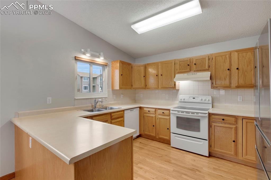 Image 7 of 27: Kitchen with light wood flooring, light countertops, a peninsula, and decor