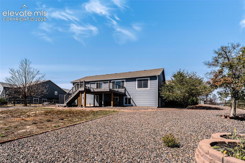Image 11 of 50: Spacious, fenced backyard with deck, patio, mature trees, grassy area, rock