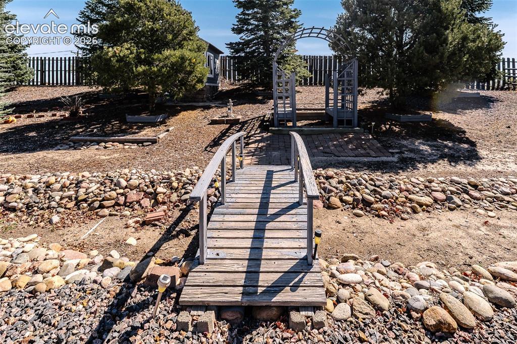 Image 46 of 50: Backyard decorative bridge and arched trellis to a garden shed behind the t