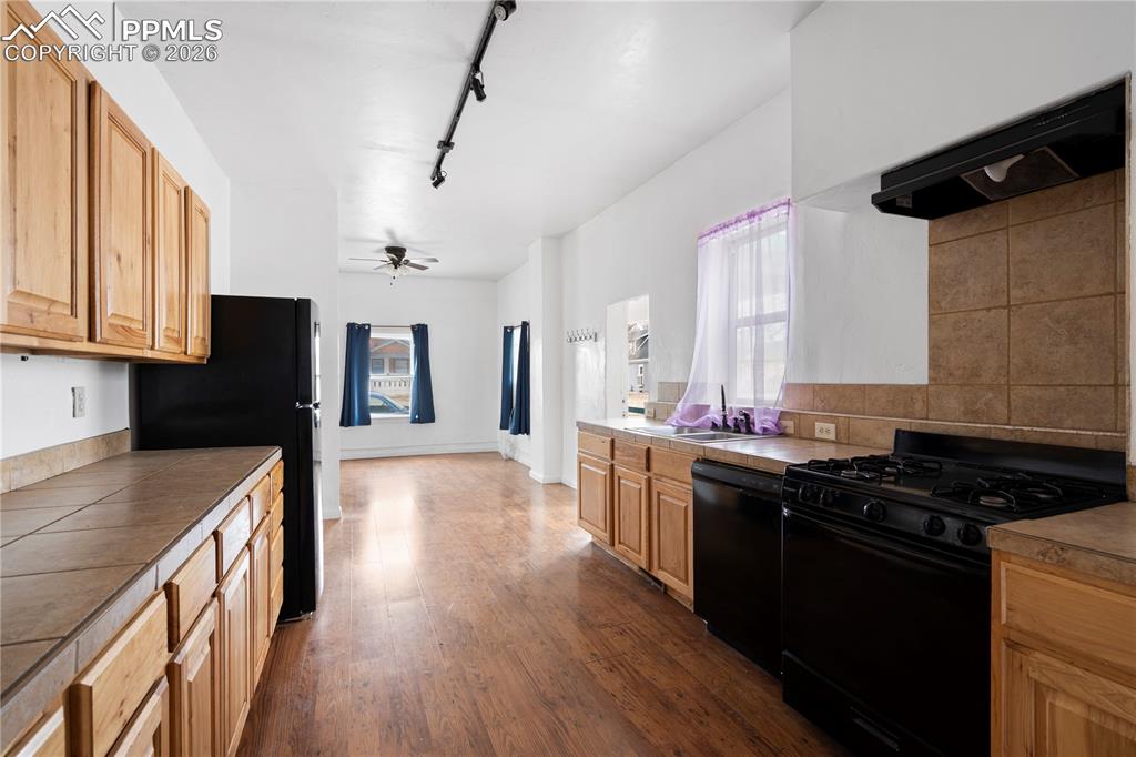 Image 4 of 21: Kitchen with black appliances, track lighting, exhaust hood, dark wood-styl