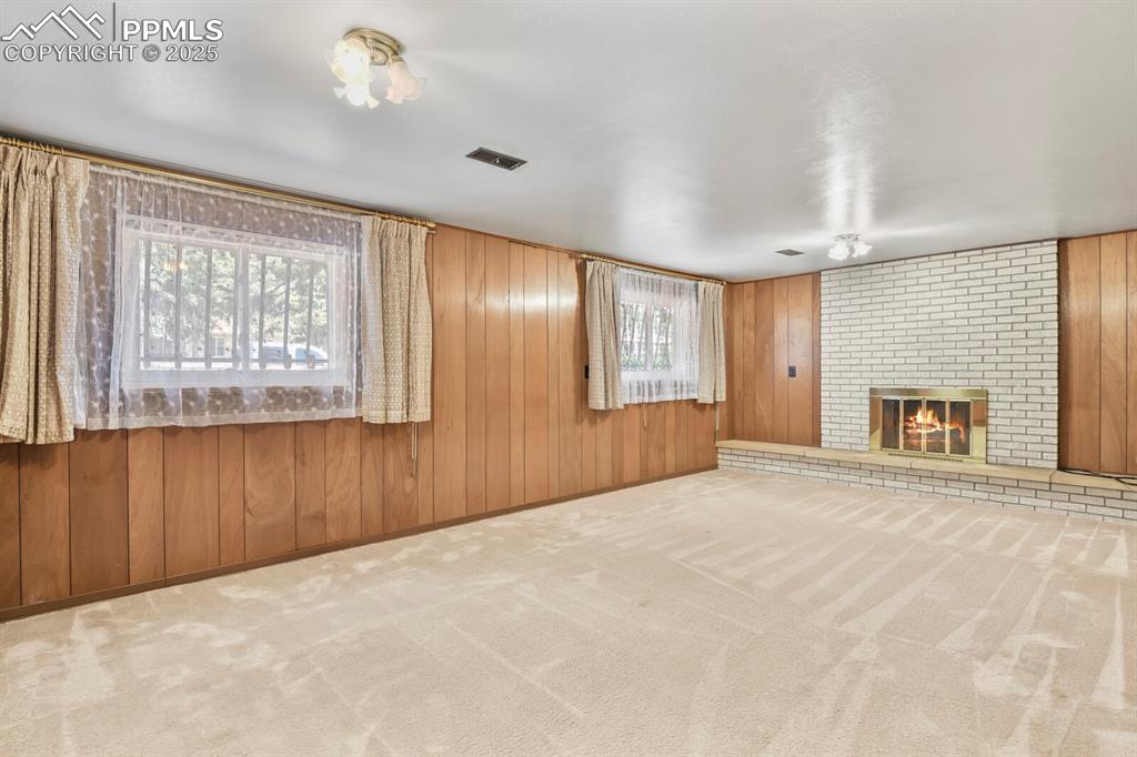 Image 18 of 26: Unfurnished living room with carpet floors, a fireplace, and wood walls