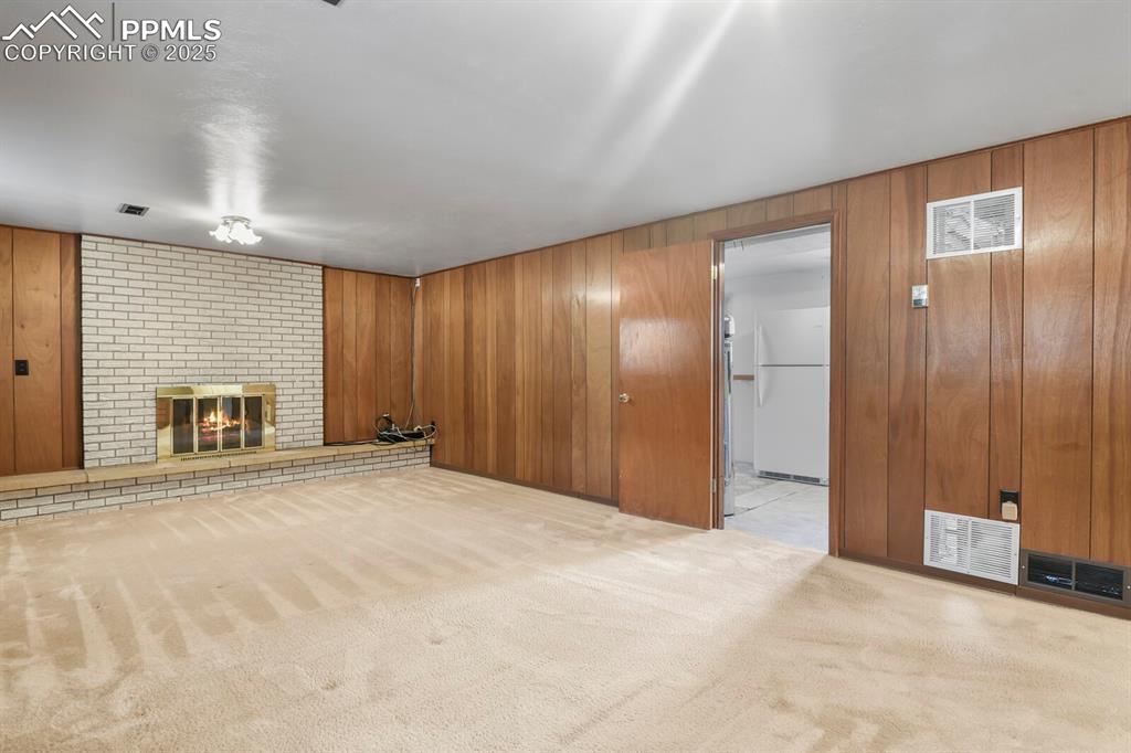 Image 20 of 26: Unfurnished living room with light carpet, wooden walls, and a brick firepl
