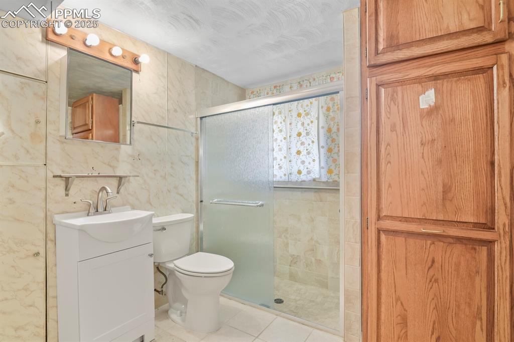 Image 22 of 26: Full bath featuring tile walls, a shower stall, vanity, and light tile patt