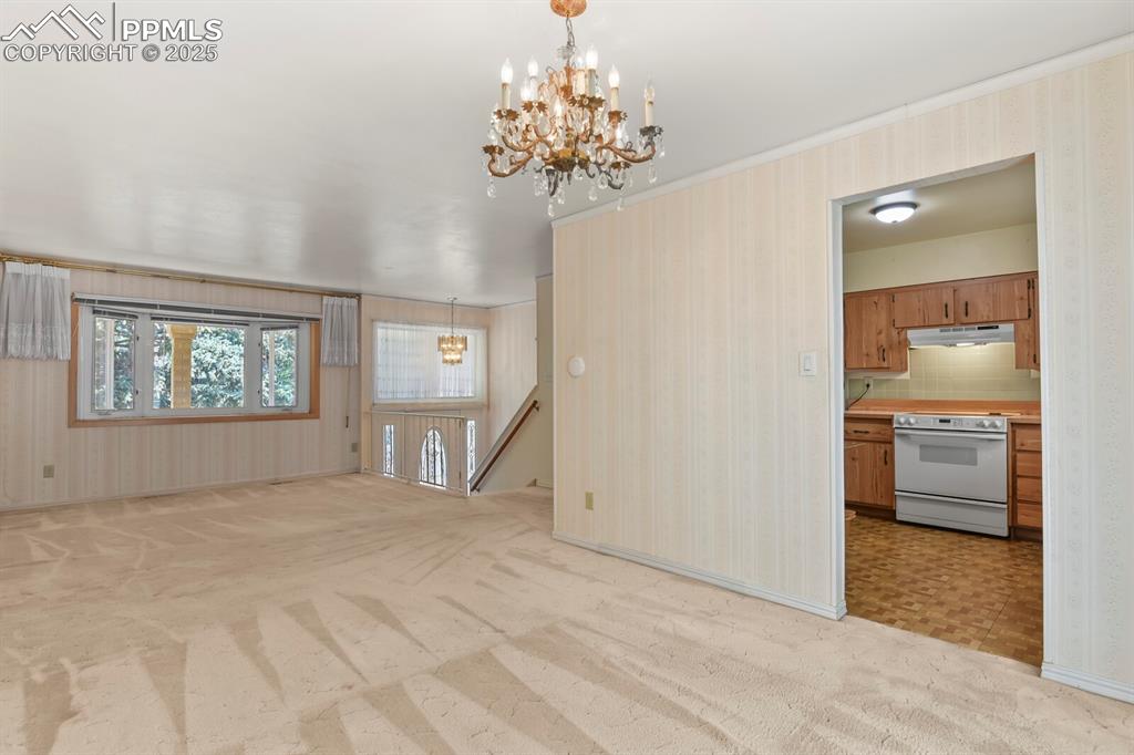 Image 9 of 26: Unfurnished living room with light carpet, wallpapered walls, and a chandel