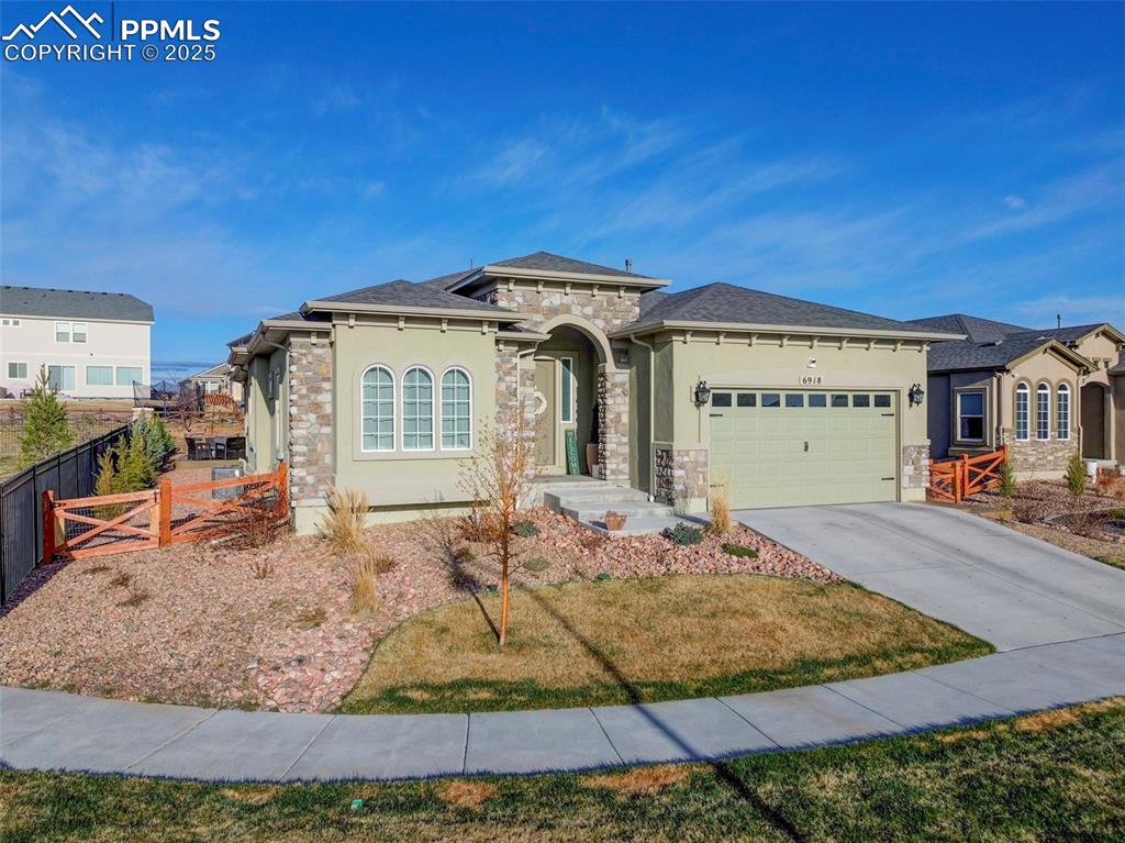 Image 2 of 50: View of front of property with stucco siding, fence, stone siding, driveway