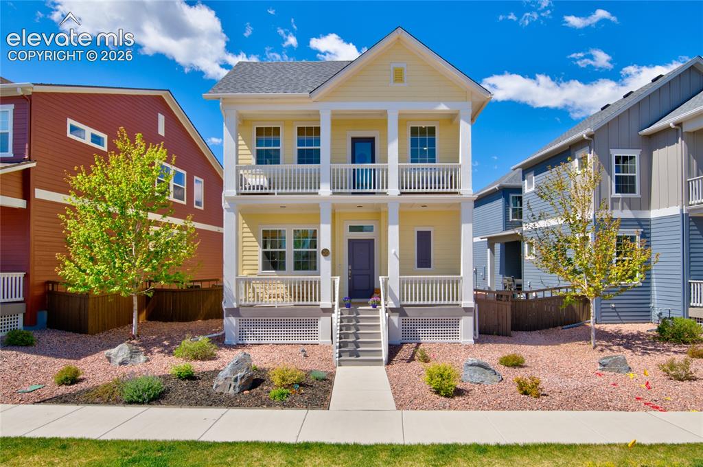 Caption: Two-story yellow residence featuring a covered front porch and upper-level balcony