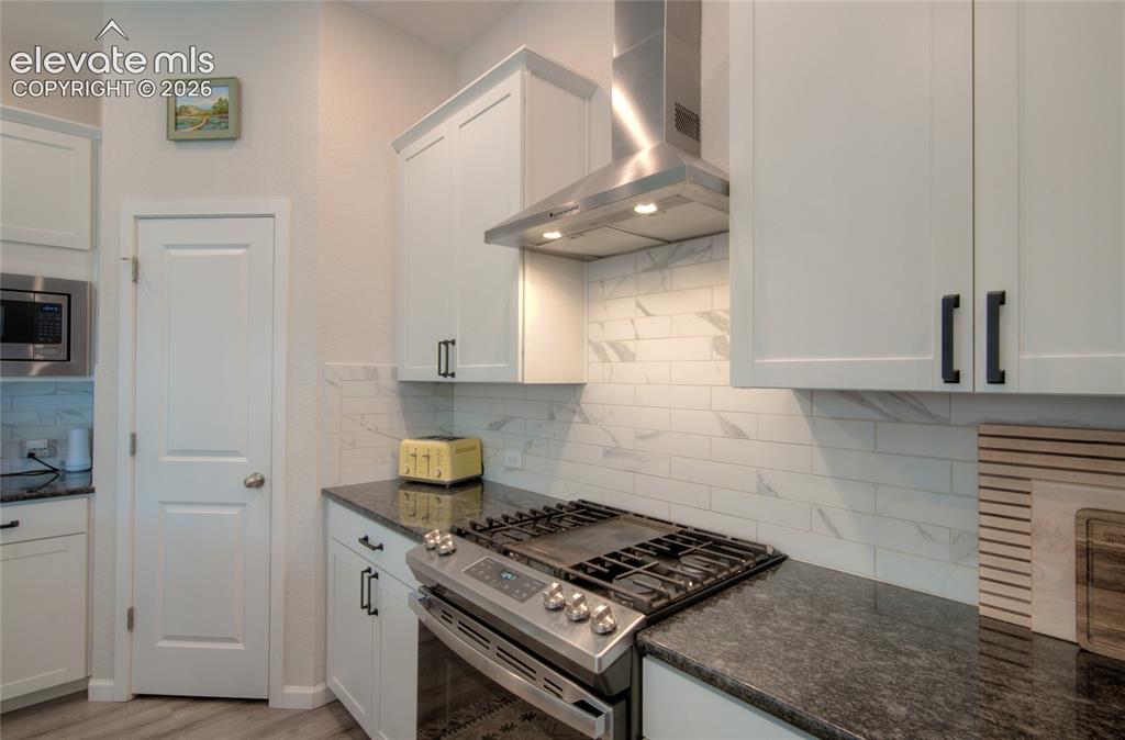 Image 11 of 35: Contemporary kitchen featuring white cabinetry, dark stone countertops, a s