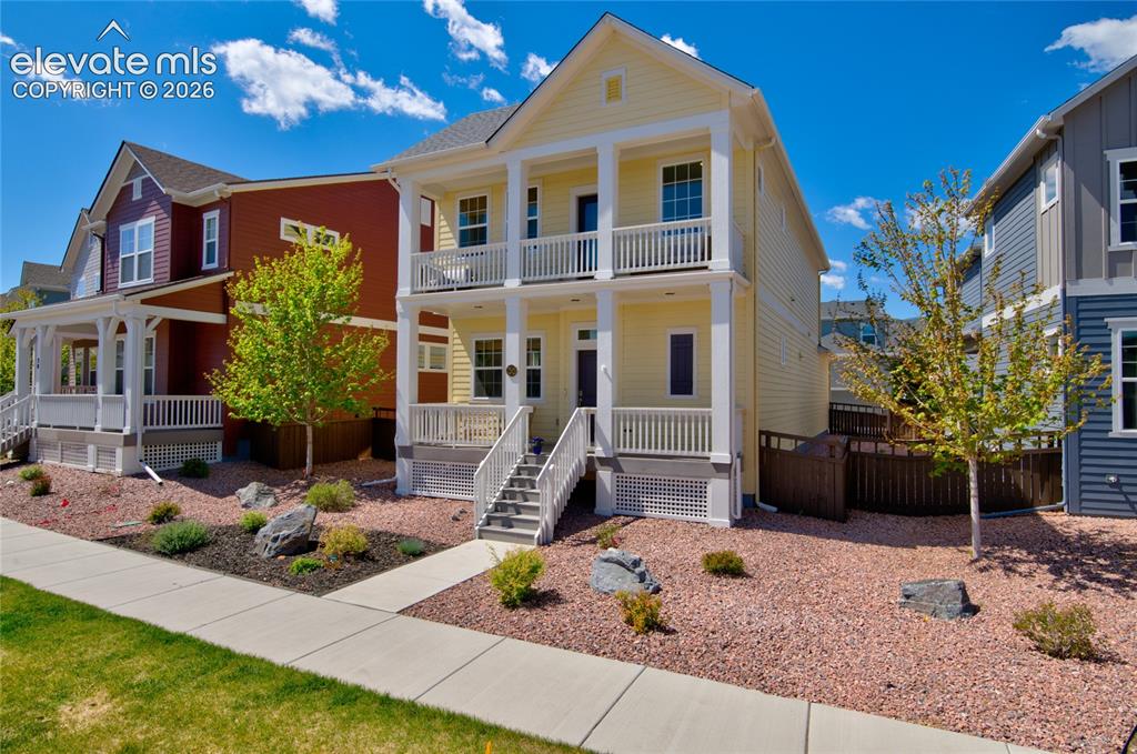Image 2 of 35: Yellow two-story residence featuring a dual-level porch with white railings