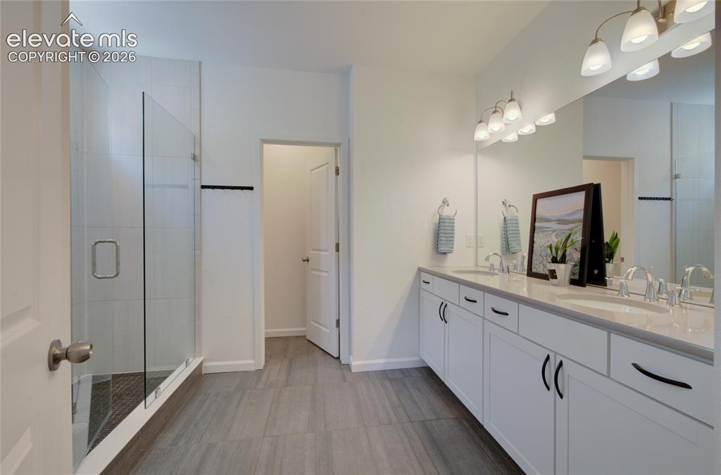 Image 23 of 35: Spacious bathroom featuring a frameless glass shower enclosure, a dual vani