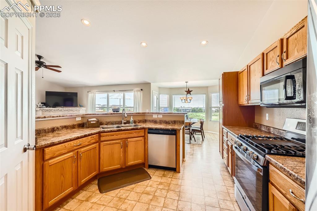Image 7 of 49: Kitchen featuring stainless steel appliances, a peninsula, brown cabinetry,