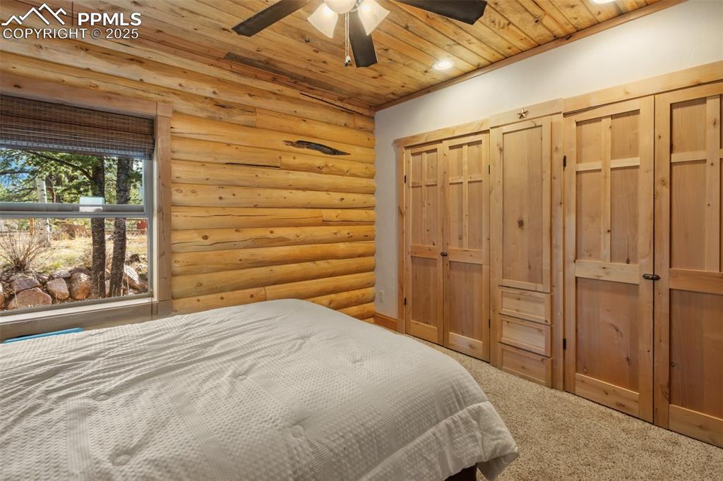 Image 30 of 46: Bedroom with log walls, a closet, wood ceiling, carpet, and a ceiling fan