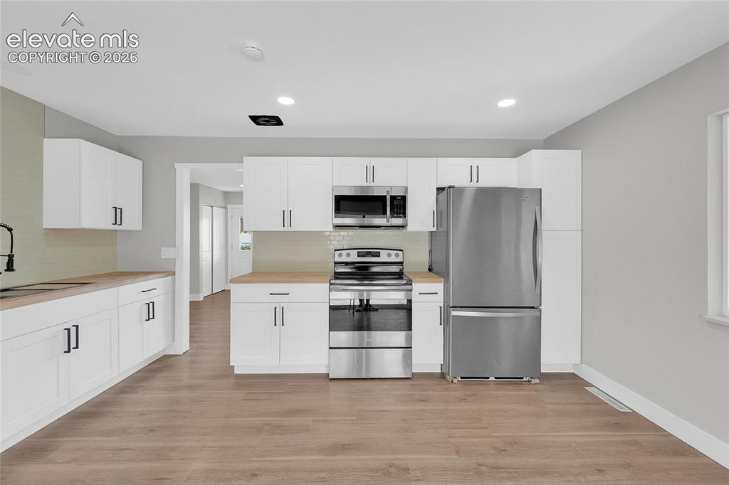 Image 10 of 27: White cabinetry with black hardware, wood-finish countertops, stainless ste