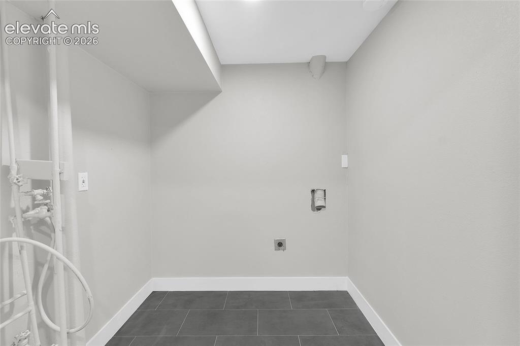 Image 17 of 27: Utility space with tile flooring, white baseboards, and wall-mounted electr