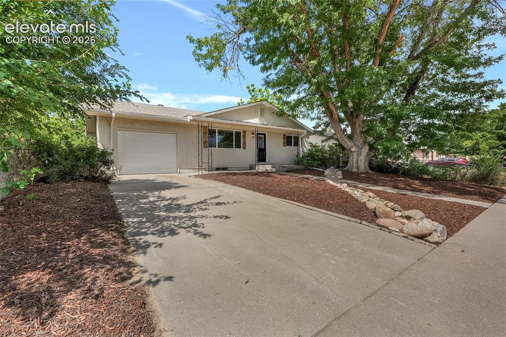 Image 2 of 27: Single-story exterior with an attached garage, paved driveway, and mature l