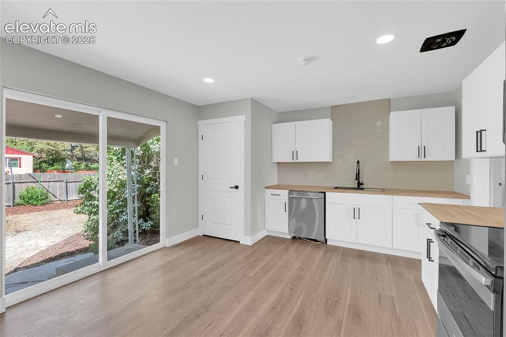 Image 9 of 27: Contemporary kitchen with white cabinetry, stainless steel dishwasher, ligh