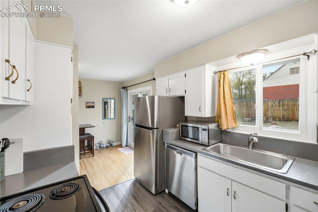 Image 4 of 47: Kitchen with white cabinets, light wood-style floors, and stainless steel a