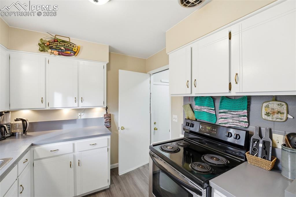 Image 6 of 47: Kitchen with range with electric stovetop, white cabinets, and light wood-s