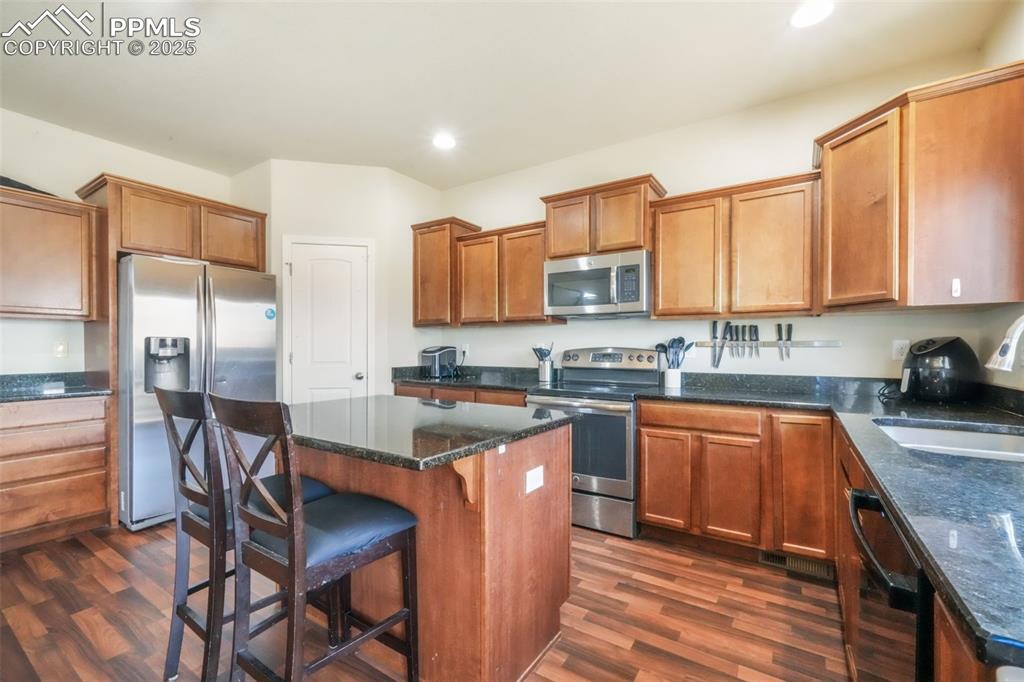 Image 13 of 48: Kitchen featuring a kitchen bar, stainless steel appliances, brown cabinetr