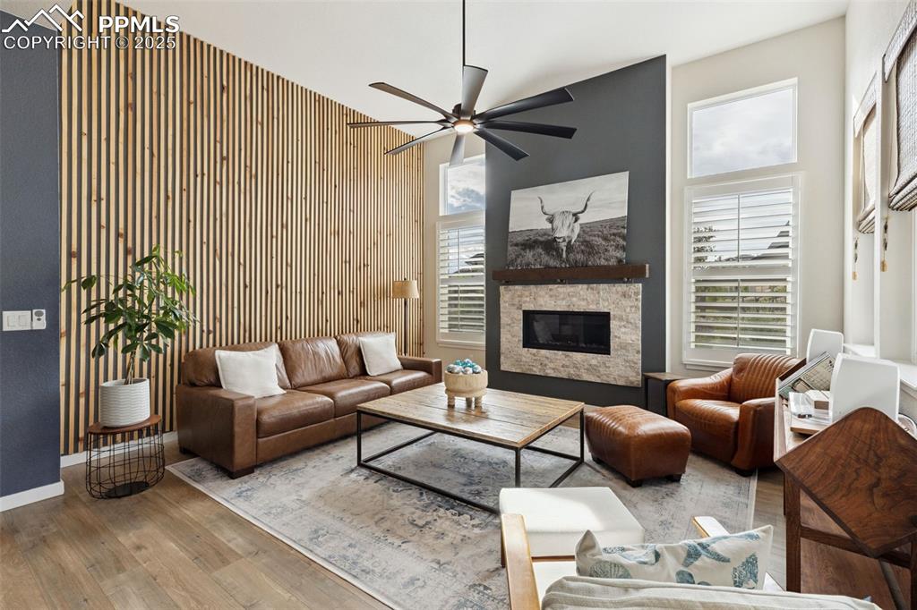 Image 14 of 49: Living area with wood finished floors, ceiling fan, a fireplace, a high cei