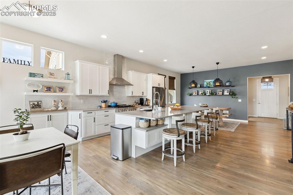 Image 16 of 49: Kitchen featuring wall chimney range hood, white cabinets, a kitchen island