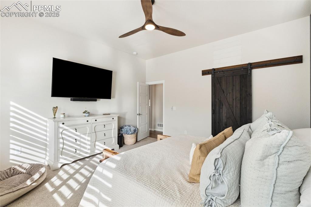 Image 25 of 49: Bedroom featuring a barn door, light carpet, and a ceiling fan
