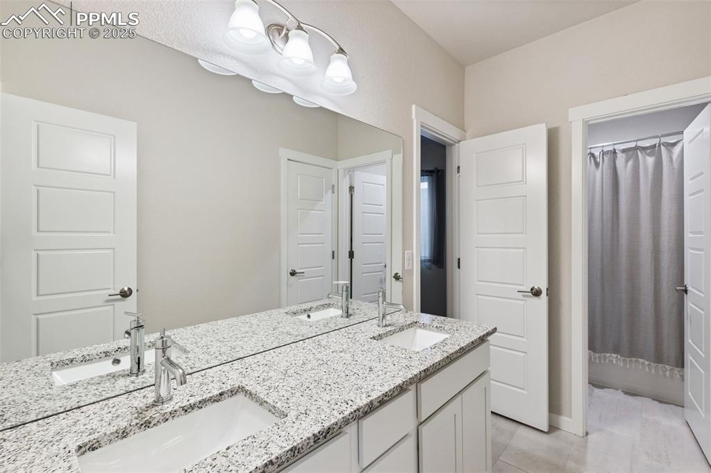 Image 31 of 49: Full bathroom with double vanity, a shower with shower curtain, and tile pa