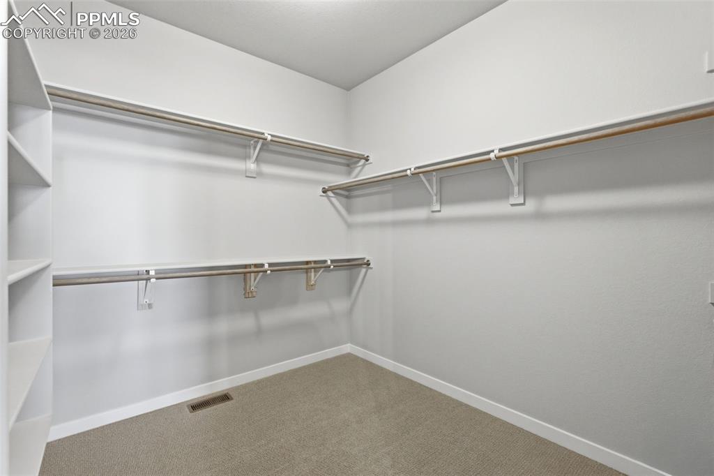 Image 26 of 48: Generous walk-in closet with built-in shelving and rod system, providing ex