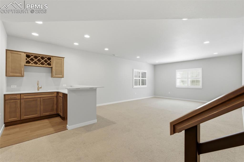 Image 27 of 48: Stylish wet bar area in basement with custom wood cabinetry and counter sea