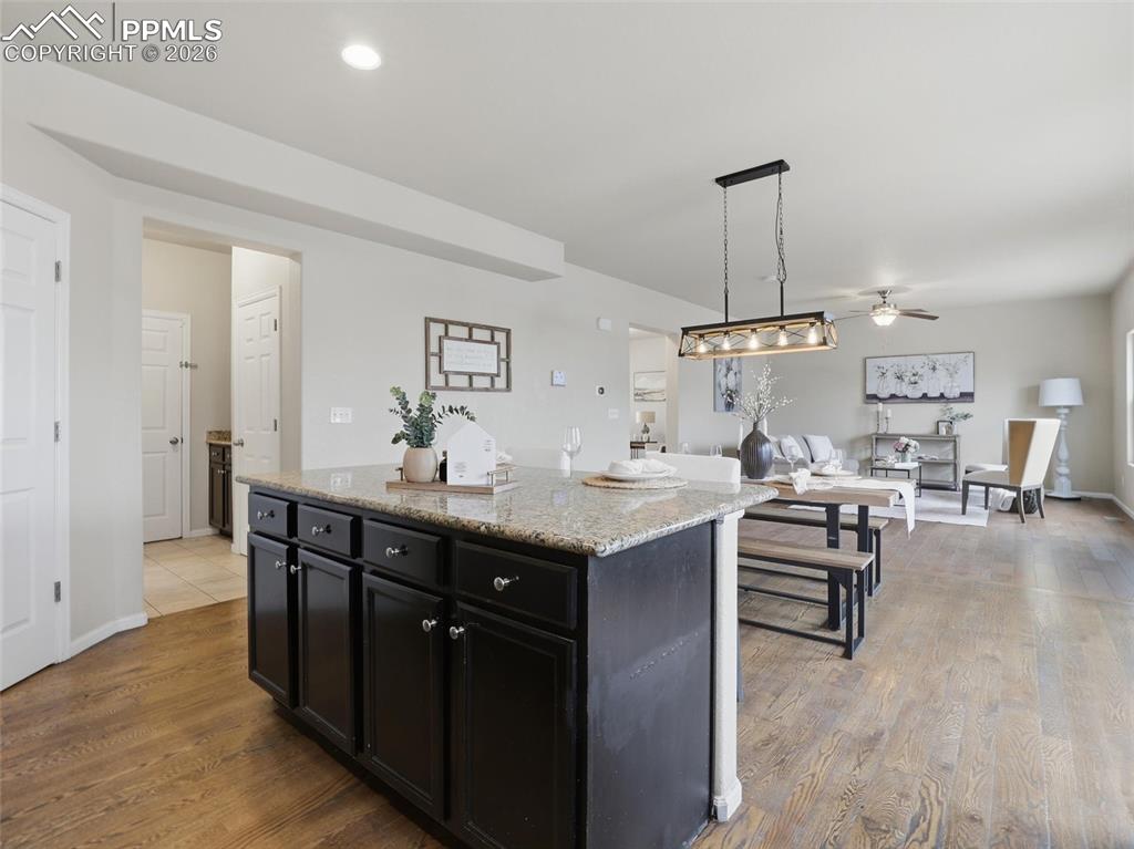 Image 14 of 45: Kitchen with dark cabinetry, decorative light fixtures, light stone counter