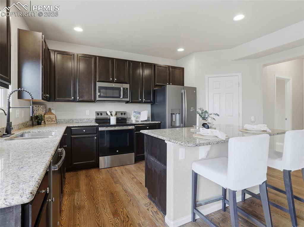 Image 15 of 45: Kitchen featuring stainless steel appliances, light stone counters, dark wo