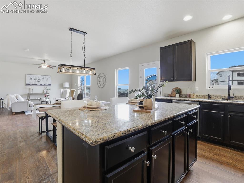 Image 18 of 45: Kitchen with dark cabinets, light stone counters, pendant lighting, open fl