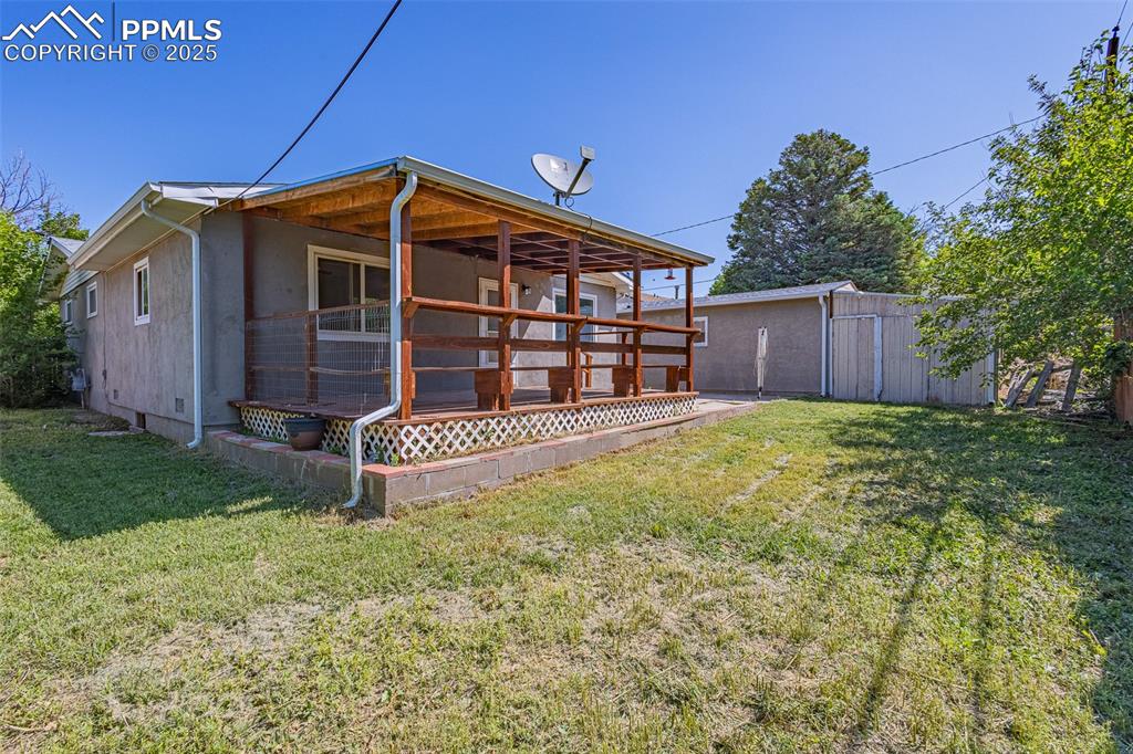 Image 15 of 24: Back of house featuring a yard, stucco siding, and an outbuilding
