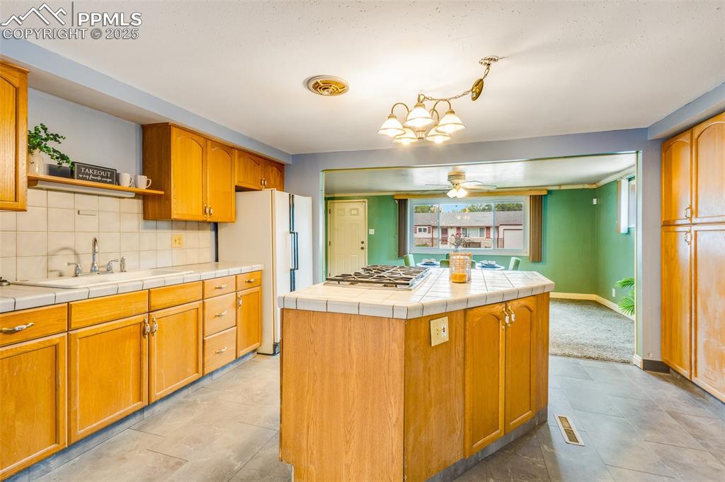 Image 5 of 24: Kitchen featuring backsplash, freestanding refrigerator, tile counters, ope