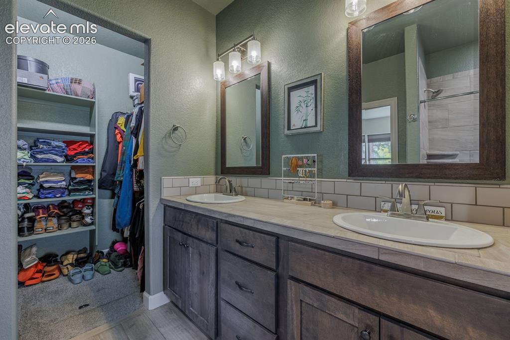 Image 11 of 16: Dual vanity with undermount sinks, wood-finish cabinetry, and subway tile b
