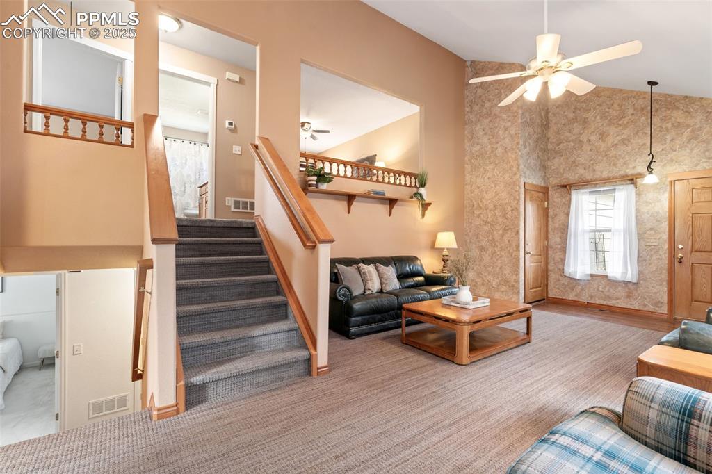 Image 10 of 36: Living room with stairway, high vaulted ceiling, ceiling fan, and light car
