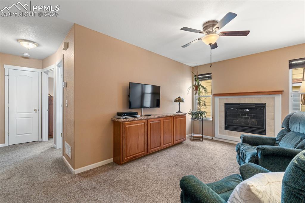 Image 15 of 36: Living area with light colored carpet, a fireplace, and a ceiling fan
