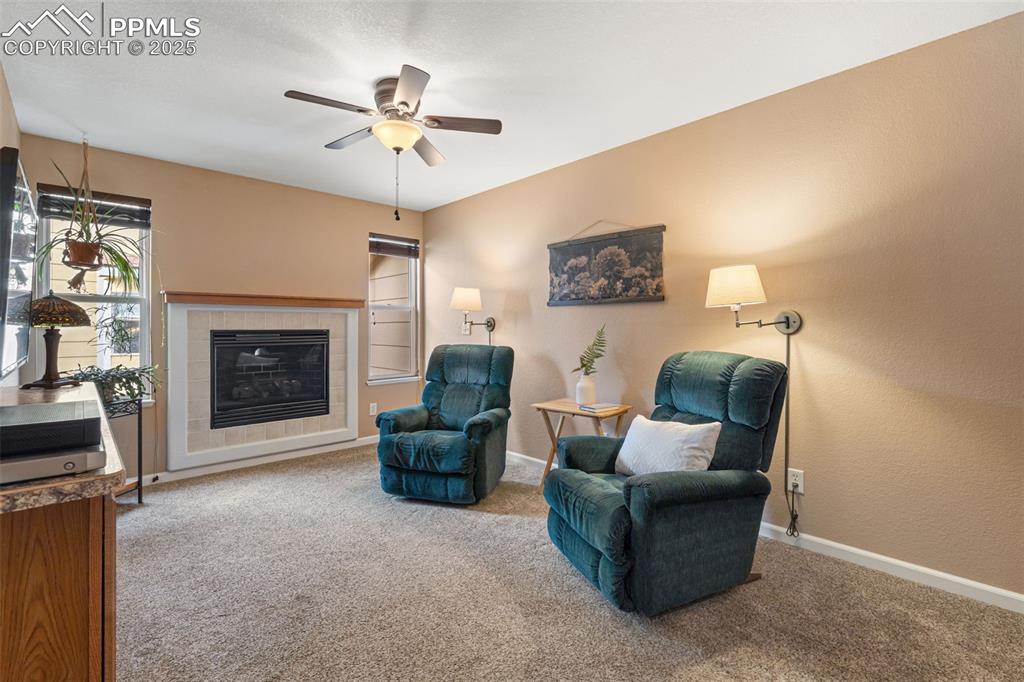 Image 16 of 36: Sitting room with light carpet, a tiled fireplace, and ceiling fan