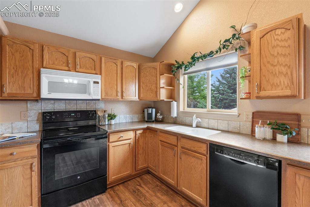 Image 5 of 36: Kitchen with black appliances, open shelves, vaulted ceiling, dark wood fin